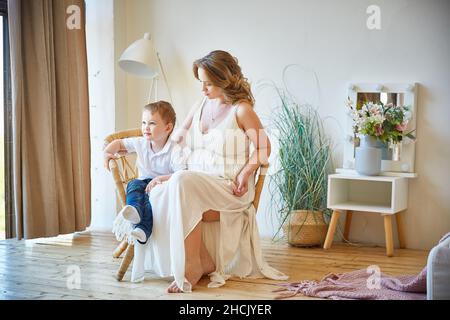 giovane donna incinta con un figlio giovane è seduta in una stanza della sua casa e pensando al futuro Foto Stock