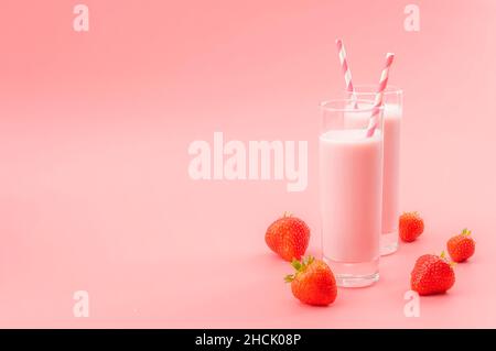 Dessert estivi rinfrescanti e calcio ricco sano bevanda tema con bicchieri di latte di fragola, cannucce a strisce e fragole sparse iso Foto Stock