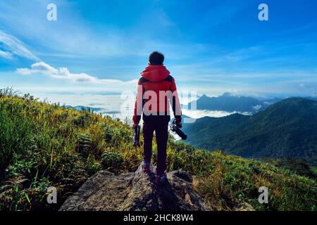 Fotografo mano tenere la fotocamera e permanente sulla cima della roccia in natura. Concetto di viaggio. Foto Stock