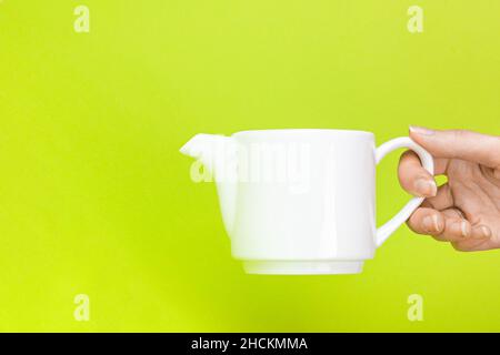 Teiera da bollitore con mano da donna su sfondo verde. Birra e tè bevente. Foto Stock