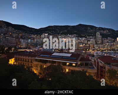 Bella vista panoramica sul centro di Monaco sulla Costa Azzurra in serata con edifici residenziali illuminati e colline. Foto Stock