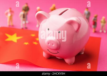 Piggy banca, bandiera cinese e giocattoli di plastica uomini su uno sfondo colorato, concetto sul tema del reddito della popolazione della Cina Foto Stock