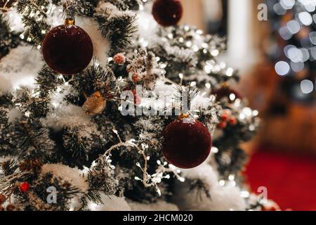 Rami di albero di Natale coperti di neve con palle di Natale di velluto rosso e ghirlanda. Nuovo anno sfondo brillante Foto Stock