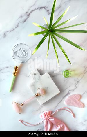 Moisturizer fatto a mano e rullo per il viso in giada verde. Asciugamano di cotone. Foglie di eucalipto esotico e gocce d'acqua su marmo bianco. Foto Stock