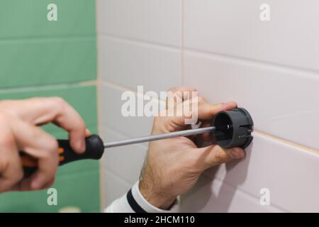 Man mano che si installa il componente in plastica del supporto della testa della doccia avvitando il chiodo con il cacciavite per fissarlo alla parete piastrellata in bagno. Ristrutturazione Foto Stock