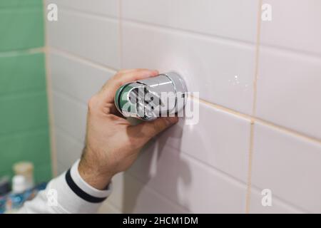 Man mano che si collega e si installa il supporto doccia con cacciavite a croce sulla parete piastrellata in bagno. Lavori di ristrutturazione nella stanza da bagno. Sporco da Foto Stock