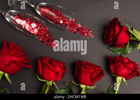 vista dall'alto delle rose rosse vicino ai bicchieri con confetti su nero Foto Stock