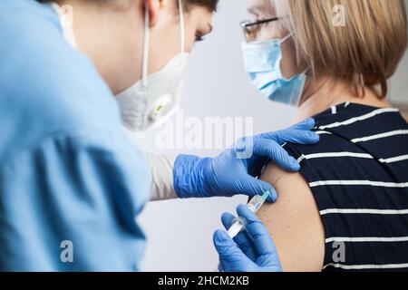 Primo piano di una giovane donna caucasica medico o medico che dà il vaccino sparato a una paziente anziana, Coronavirus immunizzazione concetto, terzo richiamo Foto Stock