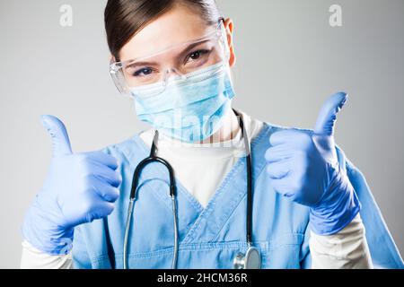 Grazioso medico caucasico femminile, allegro, ottimista e positivo operatore medico tenendo entrambi i pollici in su, paziente terapia di successo e trattamento Foto Stock