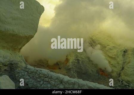 Kawah Ijen lago vulcanico cratere e tossico zolfo fumi, lavoratori estrarre lo zolfo da questa zona fumosa e portare a-80-90 Kg.-cestino pieno di zolfo sul loro Foto Stock