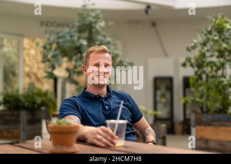 Giovane uomo caucasico seduto al tavolo e sorridente a Arhus City Foto Stock