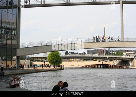 Paesaggio urbano di Berlino con vista sul fiume Sprea all'edificio Paul Loebe in estate. Persone sedute, a piedi e rilassanti in riva al fiume e sul ponte. Sfondo cielo blu chiaro. Foto Stock