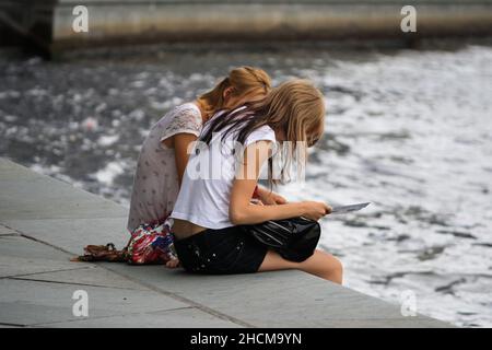 Due giovani donne europee con capelli marroni seduti e guardando la mappa dal fiume Sprea nel pomeriggio d'estate. Per concetto di viaggio e relazione. Foto Stock