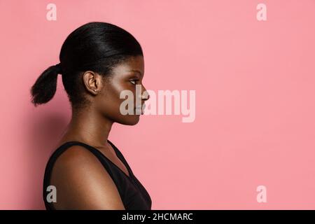 Giovane bella ragazza con pelle scura isolata su sfondo rosa studio con spazio copia per l'annuncio. Foto Stock