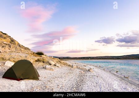 Tenda verde in piedi in spiaggia di sabbia bianca con sfondo roccioso e cielo goeroso. Campeggio in una bella e romantica località in Turchia.2020 Foto Stock