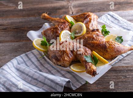 Cosce di pollo arrosto su un piatto con limone e prezzemolo a fette serviti isolati su un tavolo di legno Foto Stock