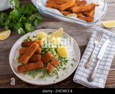 Bastoncini di pesce con piselli verdi e patate serviti con una deliziosa salsa di beshamel su un piatto Foto Stock