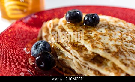 impila di crepes con mirtilli e miele su piatto rosso, fondo vaso miele, panorama Foto Stock