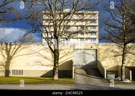 Un garage piatto allungato con un cancello. Sulla parete beige riflessi ombra di alberi. Dietro di esso un alto complesso di appartamenti. Foto Stock