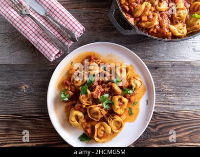 Tortellini in una deliziosa pancetta, pomodoro, salsa vegetale. Servito su un piatto bianco su sfondo rustico e tavolo in legno con spazio per la copia Foto Stock