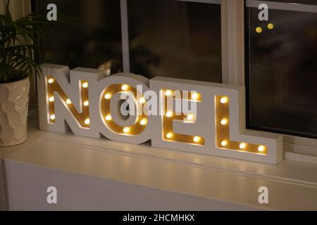 Foto di un arredamento con cartello noel illuminato di fronte a una finestra Foto Stock