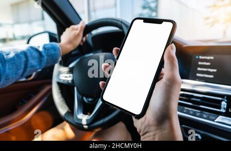 Primo piano di donna che tiene il telefono cellulare nero in mano con schermo vuoto del desktop durante la guida in auto in estate in città, immagine Mockup Foto Stock