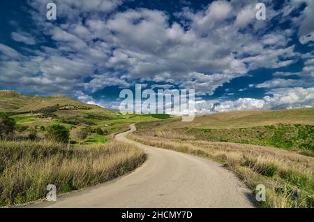 Tortuosa strada di campagna in una zona rurale della Sicilia nuvoloso e l'agricoltura collinare Foto Stock