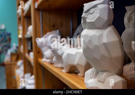 Fila di figure in ceramica grezza non finita su uno scaffale di studio in un negozio fai da te per la pittura. Foto Stock