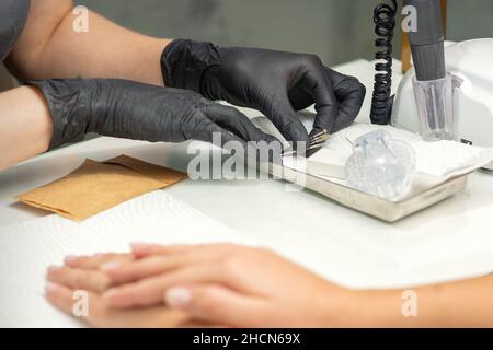 Mani in guanti neri di manicurista preparazione di speciale lima per unghie per trattamento manicure in un salone di bellezza Foto Stock