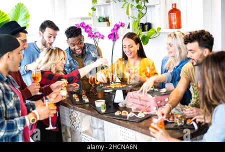Gruppo di amici che si divertono prima di cena aperitivo a buffet che bevono cocktail e mangiano spuntini - i giovani trascorrono del tempo insieme a casa Foto Stock