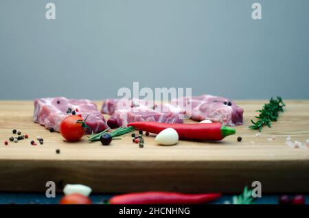 Tre succulente bistecche si trovano accanto ai peperoncini rossi e verdi, un rametto di rosmarino e aglio su un tavolo di legno. Foto Stock