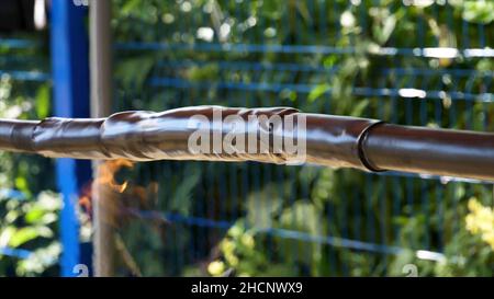 Guaina termorestringente per l'isolamento dei fili di fronte alla recinzione blu su sfondo verde di alberi. Processo di protezione dei fili, guaina termorestringente. Foto Stock