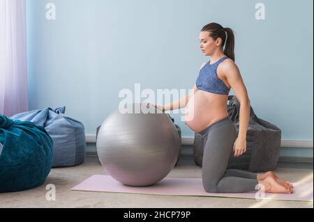 Donna europea incinta esegue esercizi con palla fitness. La madre in attesa sta facendo yoga nel 3° trimestre. Ragazza in classe in Foto Stock