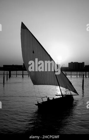 Immagine monocromatica di un dhow trainato da Lateen nelle acque del Golfo Persico, al tramonto al Louvre, all'isola di Saadiyat, Abu Dhabi, Emirati Arabi Uniti Foto Stock