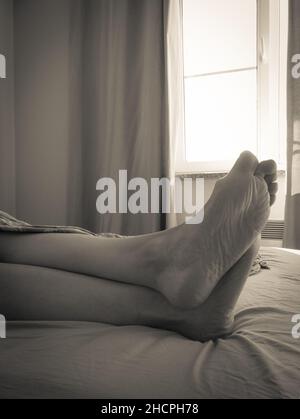 gambe femminili sul letto con copriletto Foto Stock