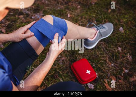 Fissazione della pioggia del ginocchio durante le escursioni. Donna ferita con fasciatura elastica del kit di pronto soccorso Foto Stock