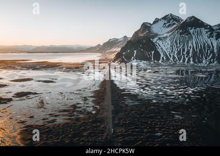 Panorama aereo di droni di strada di ghiaia al tramonto con la montagna di Vestrahorn e la spiaggia di stokksnes in Islanda sullo sfondo. Paesaggio invernale con neve e. Foto Stock