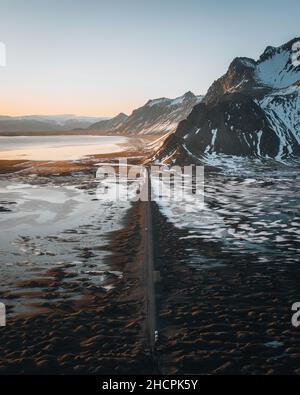 Panorama aereo di droni di strada di ghiaia al tramonto con la montagna di Vestrahorn e la spiaggia di stokksnes in Islanda sullo sfondo. Paesaggio invernale con neve e. Foto Stock