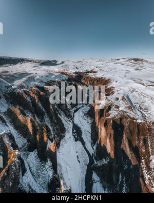 Veduta aerea del drone del canyon di Fjadrargljufur e del fiume Fjadra in inverno. Neve bianca e fiume blu. Islanda nei pressi di Reykjavik. Foto Stock