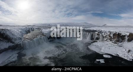 Colpo di drone della cascata di Godafoss, Islanda, preso da un angolo alto. Vista aerea della potente cascata, del fiume e delle rocce innevate. Fine autunno Foto Stock