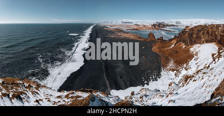 Vista dal faro di Dyrholaey in Islanda con vista sulla spiaggia di sabbia nera sottostante durante l'inverno con neve e bel tempo di sole. Foto Stock