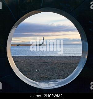 Roker Pier e Lighthouse catturati attraverso il centro di una scultura contemporanea su Roker Beach a Sunderland, Tyne and Wear. Foto Stock