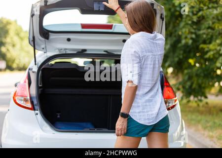 Giovane conducente donna che chiude il bagagliaio dell'auto a noleggio Foto Stock