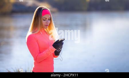 Giovane donna sportiva che controlla il suo tracker fitness sullo smartphone durante la corsa mattutina Foto Stock