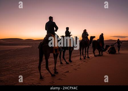 Carovana di cammelli con turisti che attraversano la sabbia nel deserto Foto Stock