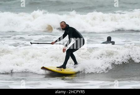 Una pagaia bordo surfs un'onda nel mare al largo della spiaggia di Bournemouth in Dorset. Il Regno Unito potrebbe vedere la vigilia di Capodanno più mite in record, con il sole in alcune zone, dopo quello che probabilmente sarà uno dei Decembers più nulle mai. Ma nonostante il sole, i rivelatori in alcune parti del Regno Unito dovranno rinforzarsi per le docce pesanti la sera. Data immagine: Venerdì 31 dicembre 2021. Foto Stock