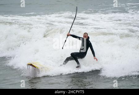 Una pagaia bordo surfs un'onda nel mare al largo della spiaggia di Bournemouth in Dorset. Il Regno Unito potrebbe vedere la vigilia di Capodanno più mite in record, con il sole in alcune zone, dopo quello che probabilmente sarà uno dei Decembers più nulle mai. Ma nonostante il sole, i rivelatori in alcune parti del Regno Unito dovranno rinforzarsi per le docce pesanti la sera. Data immagine: Venerdì 31 dicembre 2021. Foto Stock