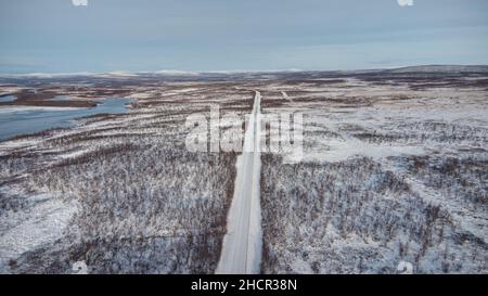 Arido paesaggio inospitale della Lapponia, Finlandia settentrionale. Vista sul lago, sulle montagne e sulla strada principale sotto una copertura di neve e ghiaccio. Paesaggio intorno a. Foto Stock