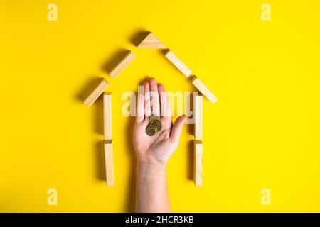 Vista dall'alto della mano del bambino close up blocchi di costruzione che mostrano soldi mince, casa, capanna di legno Foto Stock