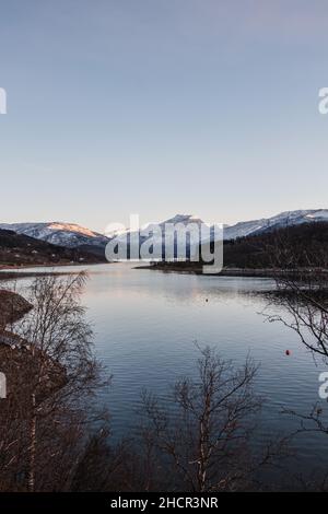 Colline innevate che si affacciano sul lago Rombaken vicino alla città di Narvik nella Norvegia settentrionale, Scandinavia. Gli ultimi scivolini di tramonto cadono sul molo Foto Stock